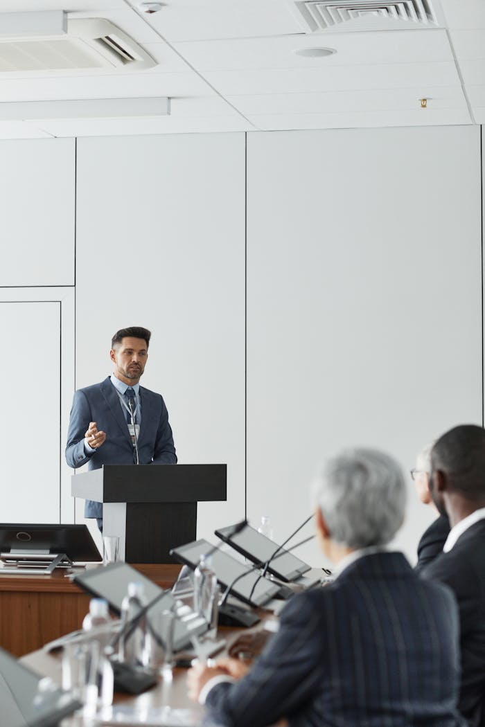 A man in a blue suit giving a presentation at a conference podium indoors.